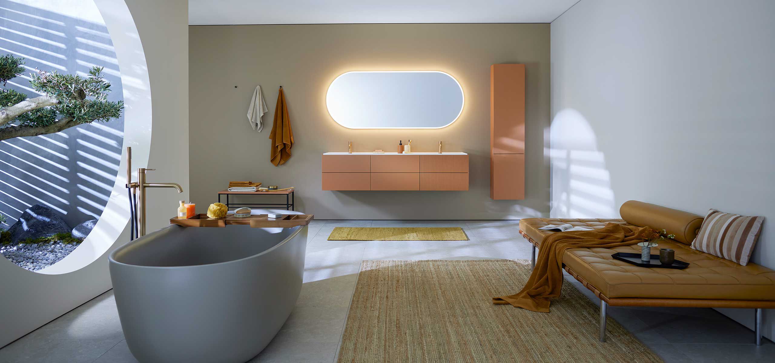 salle de bain avec baignoire grise en saillie, meubles de salle de bain en terracotta et miroir lumineux ovale