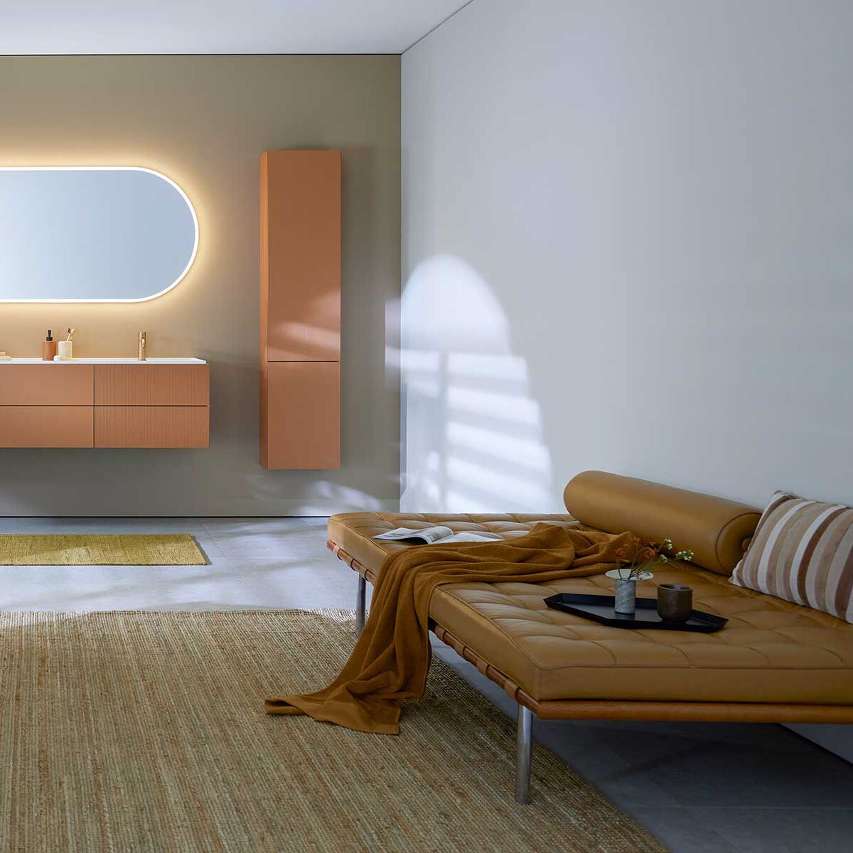 Il negozio online di Sanitas Troesch spiegato in breve bagno con vasca autoportante grigia, mobili da bagno in terracotta e specchio ovale chiaro