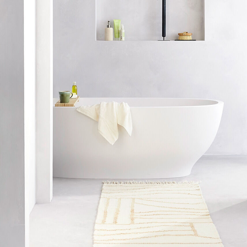 freistehende weisse badewanne hinter gelb weissem teppich