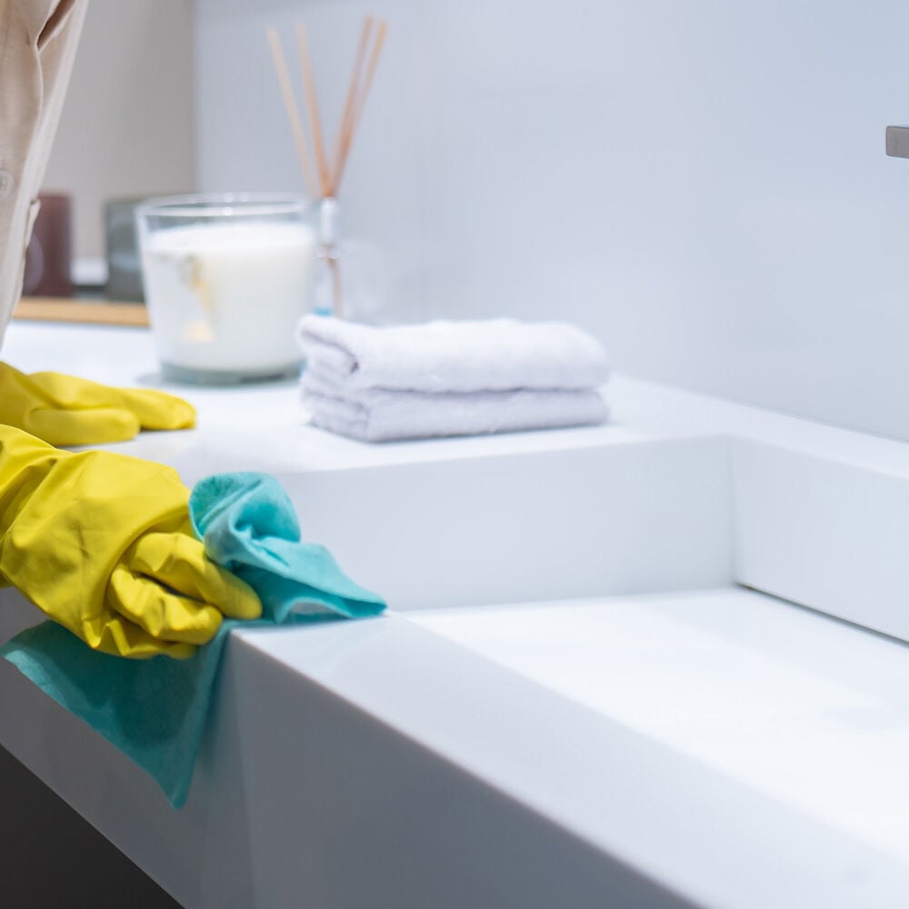 Welches Putzmittel für welche Badezimmer-Oberfläche? frau putzt waschtisch grüner lumpen und gelbe gummihandschuhe