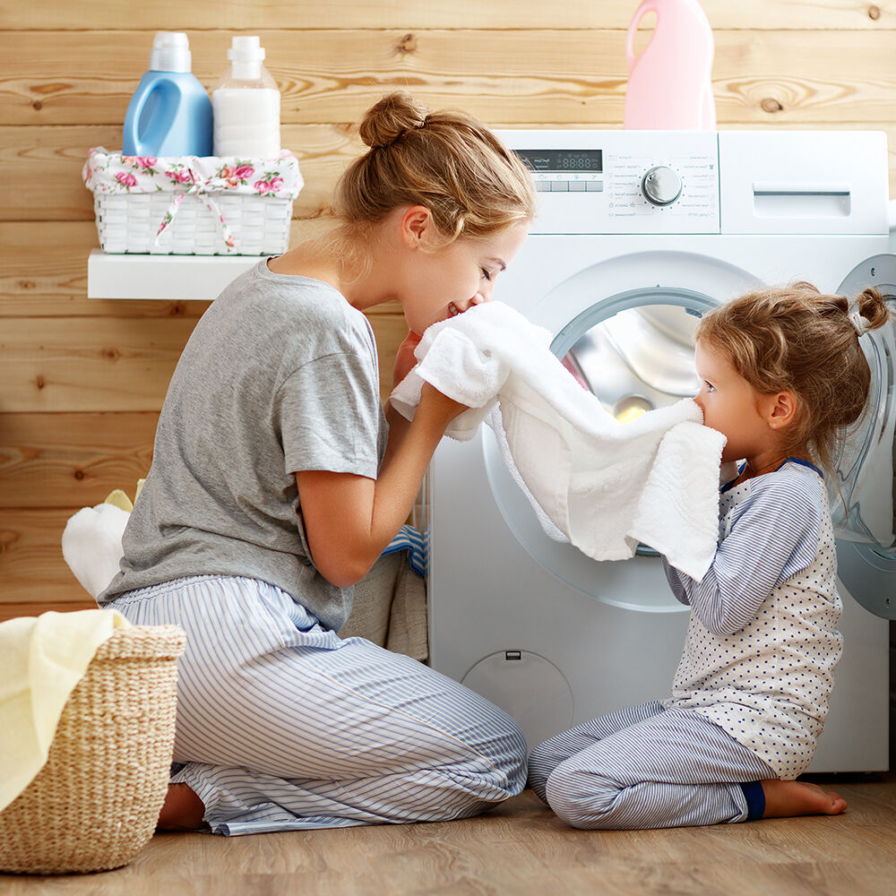 Mutter riecht mit ihrem kleinen Mädchen an frischgewaschener Kleidung